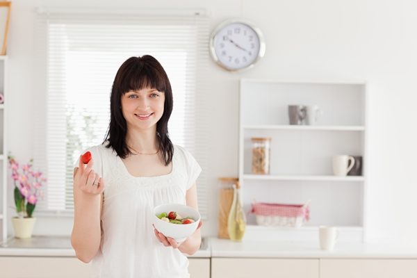 charming-brunette-female-eating-a-cherry-tomato-while-holding-a